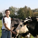 Jeune éleveur souriant proche des vaches Prim'Holstein dans les prés, champs, prairies
