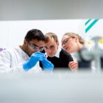 Trois ingénieurs dans laboratoire regardent un échantillon, gants bleus